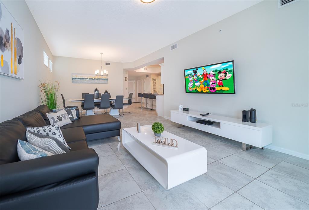 A living room with a black sectional sofa, white coffee table, and wall-mounted television — 3180 PARADOX CIRCLE UNIT 108, KISSIMMEE, FL