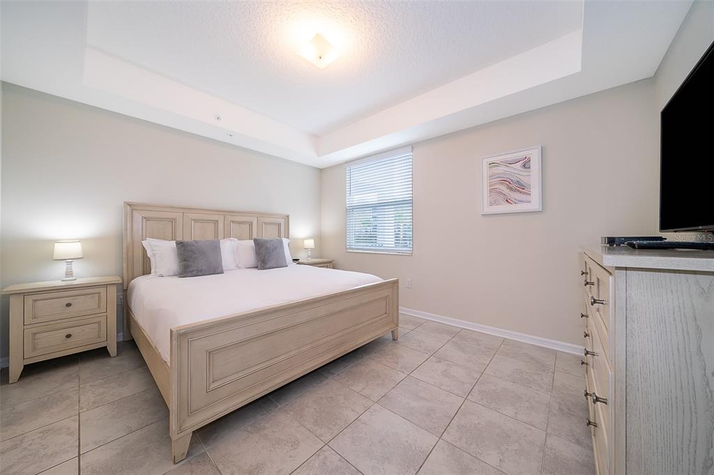 A bedroom features a light wood bed frame, tile flooring, and a tray ceiling — 3180 PARADOX CIRCLE UNIT 108, KISSIMMEE, FL