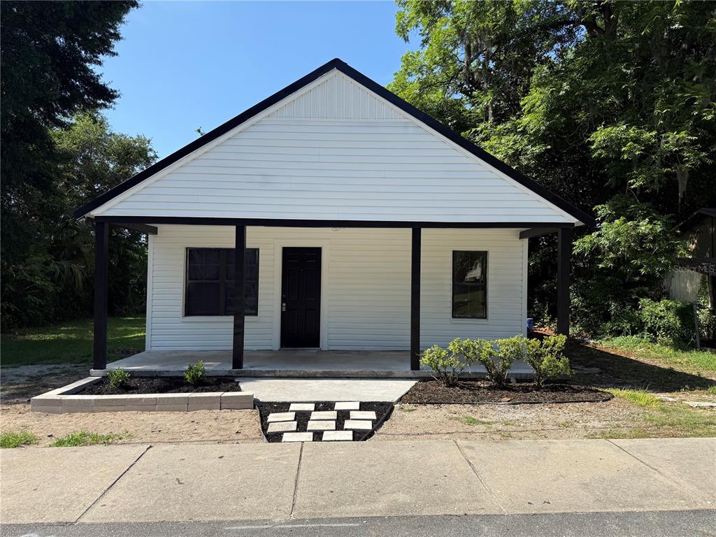A white house with a black-trimmed porch and a small front garden sits behind a sidewalk — 1018 SW 2ND STREET, OCALA, FL