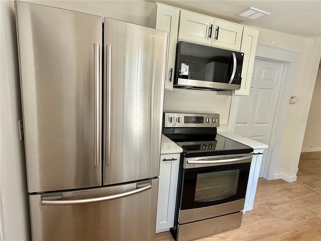 A kitchen features stainless steel appliances, white cabinets, and light wood-look flooring — 1018 SW 2ND STREET, OCALA, FL