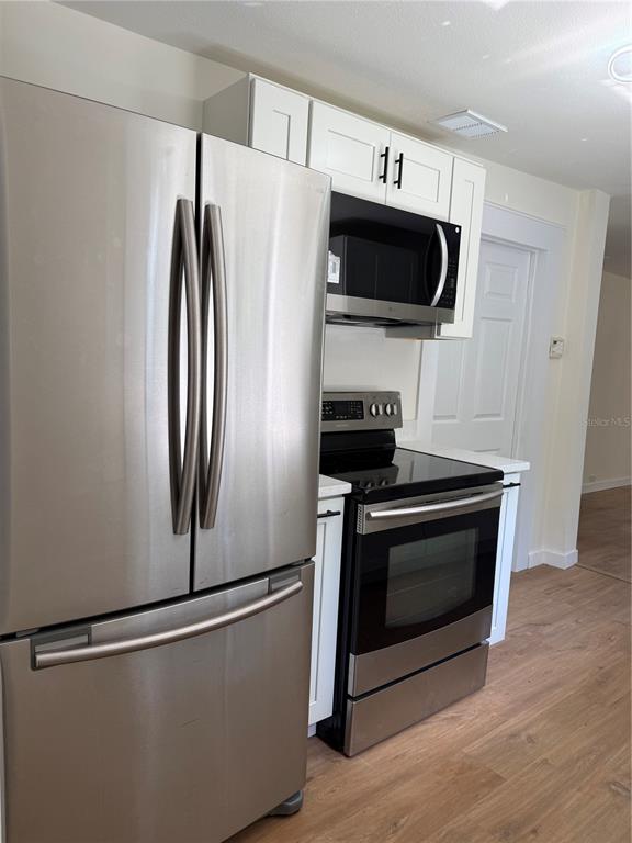 A kitchen features stainless steel appliances, white cabinets, and light wood-look flooring — 1018 SW 2ND STREET, OCALA, FL