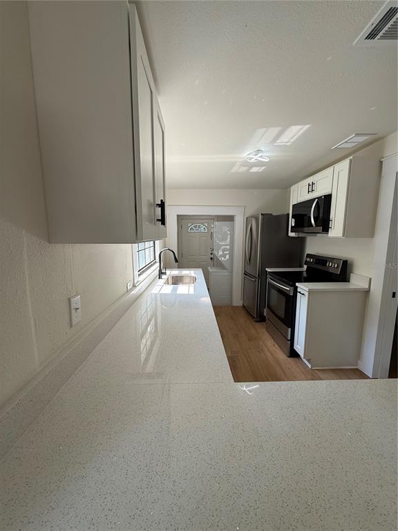 A kitchen features white cabinets, quartz countertops, stainless steel appliances, and light wood-look flooring — 1018 SW 2ND STREET, OCALA, FL
