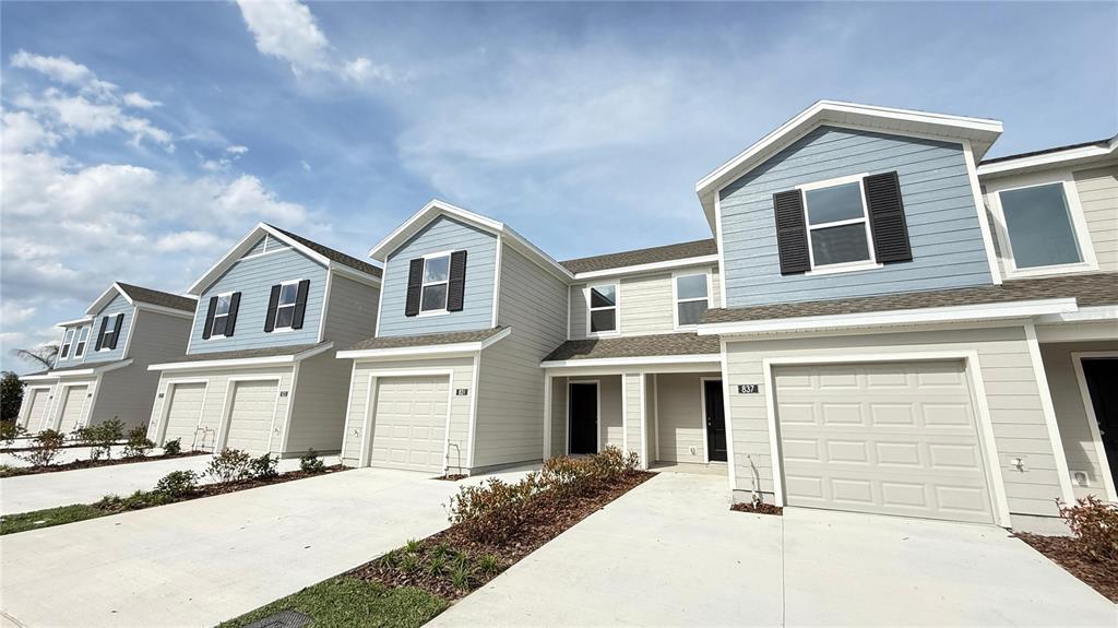 A row of modern townhouses features light-colored siding, blue accents, and attached garages — 837 LYNX STREET, DAVENPORT, FL