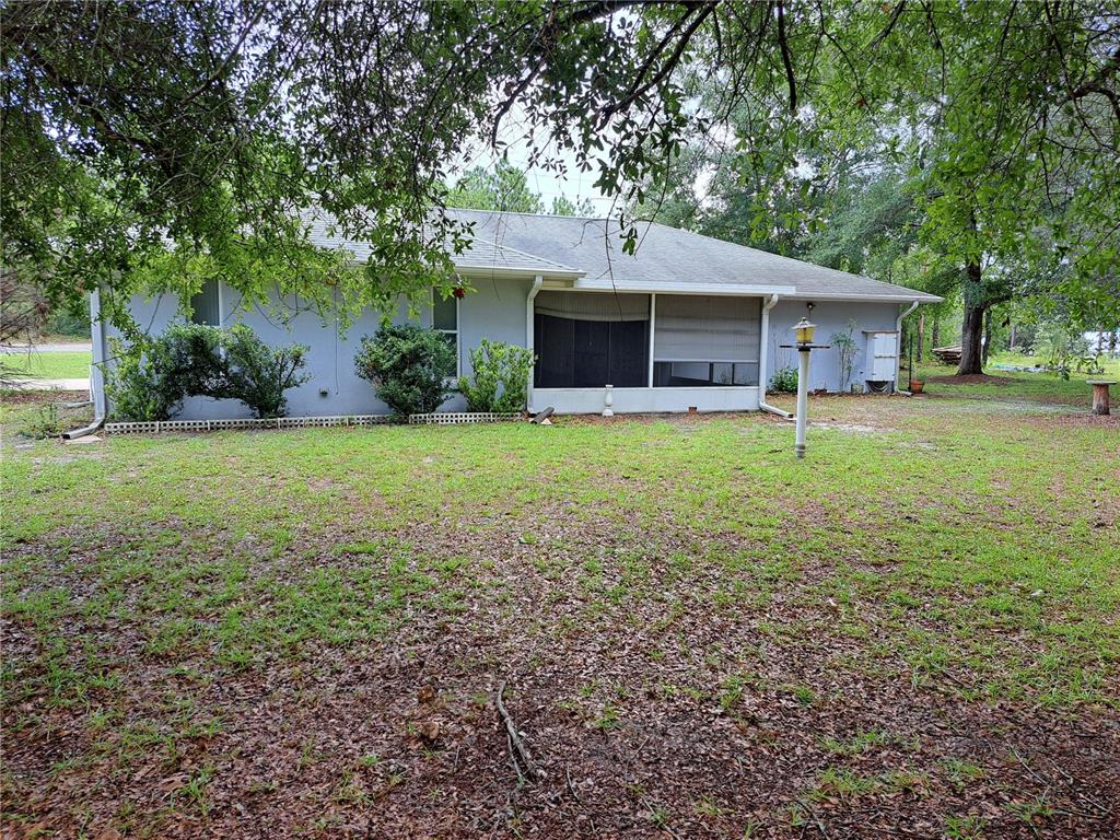 A gray single-story house features a screened-in porch and a large, tree-shaded grassy yard — 2692 W HAMLET PLACE, DUNNELLON, FL