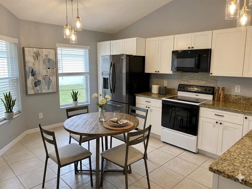 A kitchen with white cabinets, granite countertops, a black refrigerator, and a small dining table — 82 LAKEPOINTE CIRCLE UNIT 82, KISSIMMEE, FL