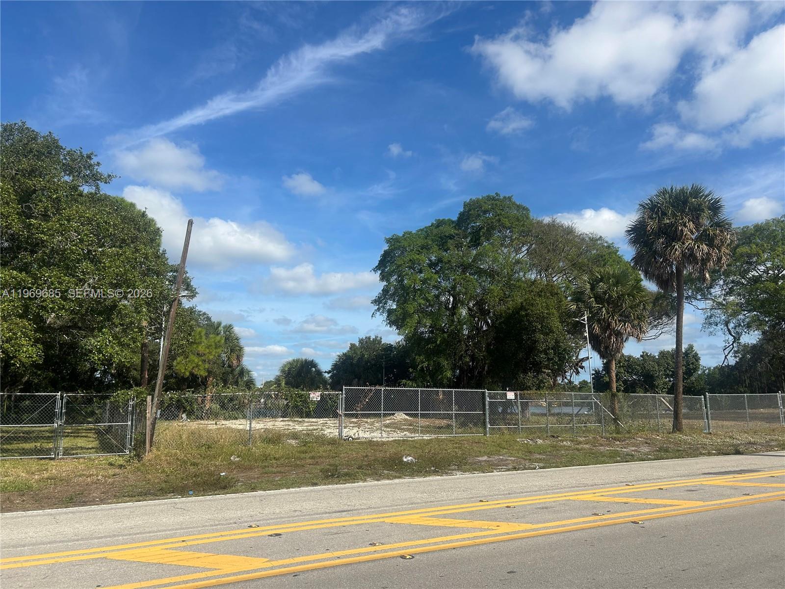 A chain-link fence encloses a vacant, sandy lot with trees under a blue sky — 2541 SW 36th St, Dania Beach FL 33312, DANIA BEACH, FL