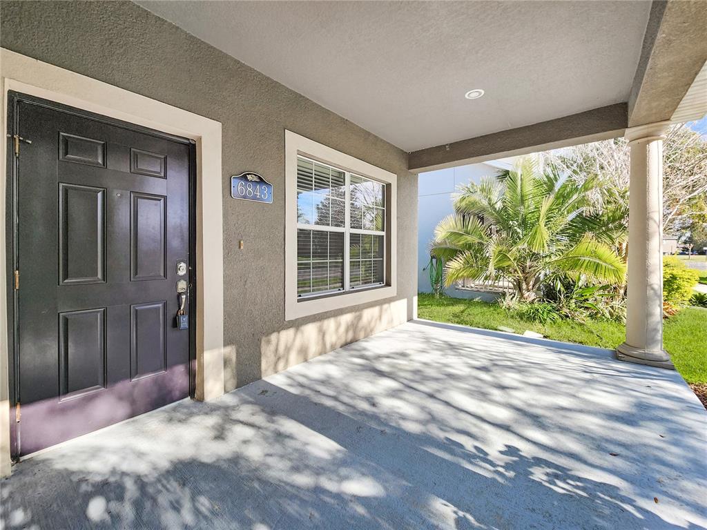 A covered front porch features a dark door, a window, and a concrete floor — 6843 POINT HANCOCK DRIVE, WINTER GARDEN, FL