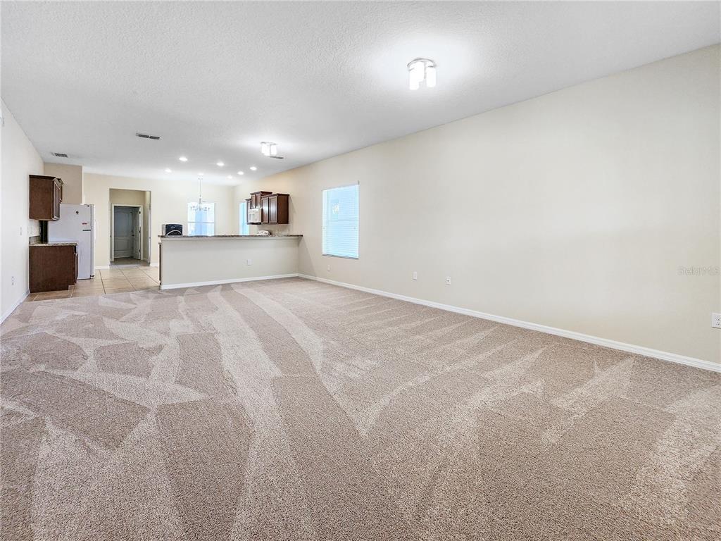 A spacious living room with beige carpet opens to a kitchen with a breakfast bar — 6843 POINT HANCOCK DRIVE, WINTER GARDEN, FL