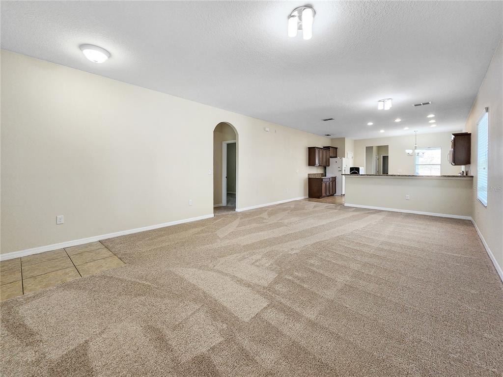 A spacious living room with beige carpet, an arched doorway, and an open kitchen beyond — 6843 POINT HANCOCK DRIVE, WINTER GARDEN, FL