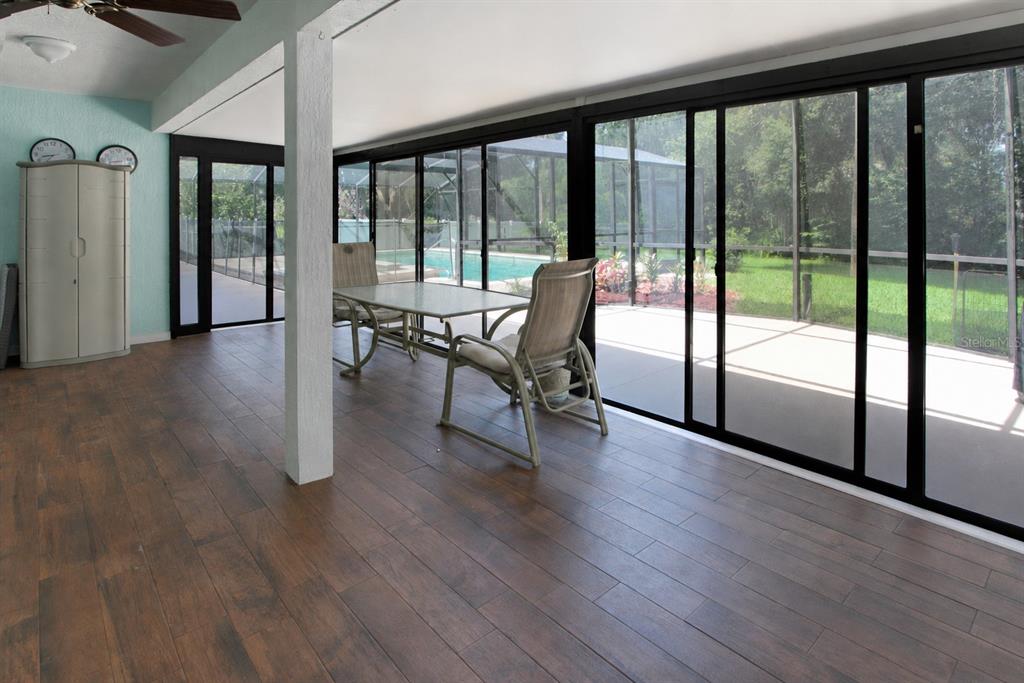 A sunroom with wood-look tile flooring features a dining set and large sliding glass doors — 34205 PARK LANE, LEESBURG, FL