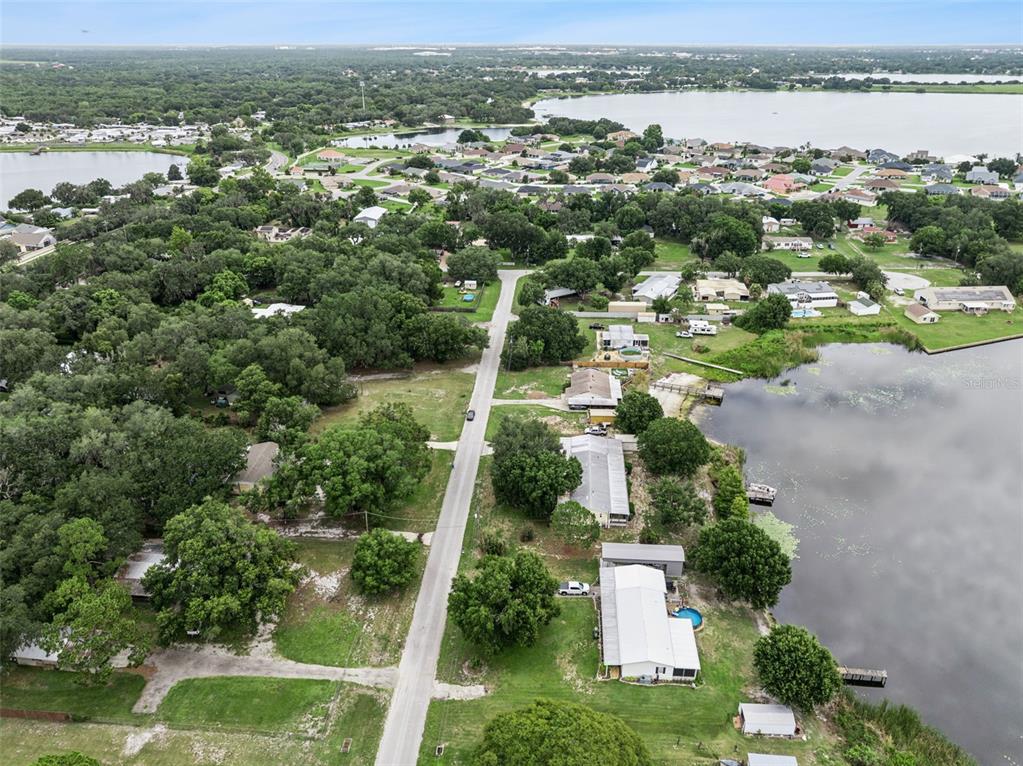 An aerial view shows a residential street lined with houses and trees near a lake — 126 BERMUDA COURT, WINTER HAVEN, FL