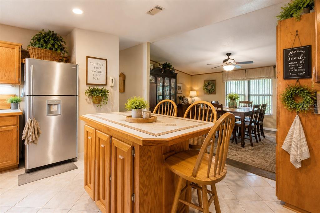 A kitchen with oak cabinets, a tiled island, and an adjacent dining area — 126 BERMUDA COURT, WINTER HAVEN, FL