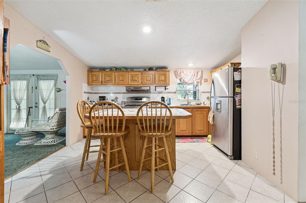 A kitchen features a central island with two wooden chairs, tile flooring, and stainless appliances — 126 BERMUDA COURT, WINTER HAVEN, FL