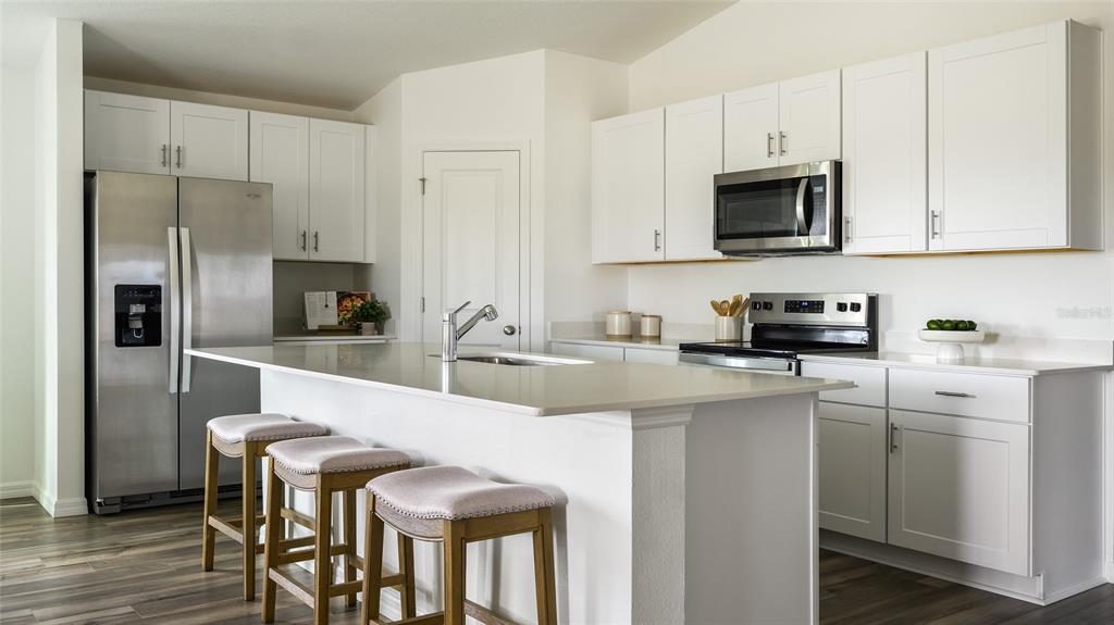 A modern kitchen features white cabinets, stainless steel appliances, a quartz island, and wood flooring — 31670 OYSTER TRELLIS LANE, WESLEY CHAPEL, FL