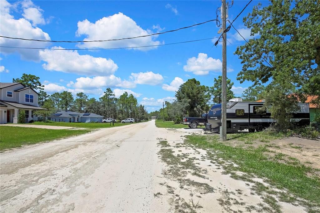 A dirt road leads through a residential neighborhood with houses, trees, and a parked camper — 16126 MEDRICK ROAD, BROOKSVILLE, FL