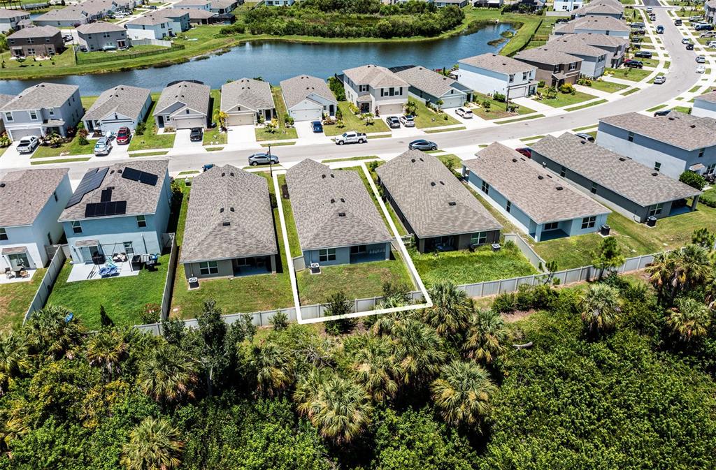 An aerial view shows a row of suburban houses with fenced backyards bordering a wooded area — 5185 ROCKY COAST PLACE, PALMETTO, FL