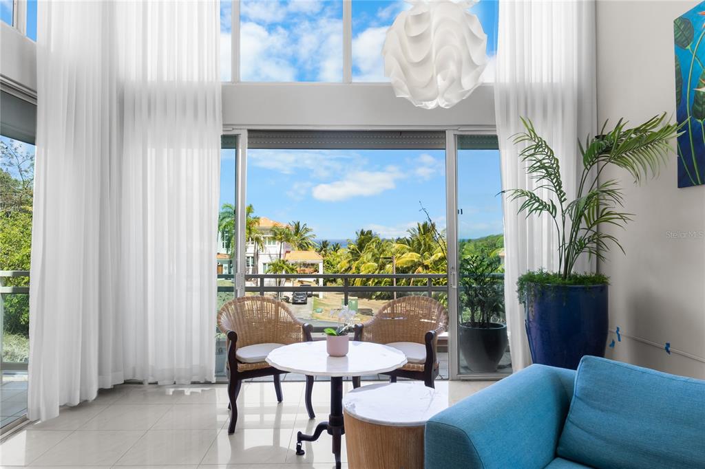 A bright living room features floor-to-ceiling windows, white curtains, wicker chairs, and a balcony view — 1 SHELL CASTLE CLUB CLUB, HUMACAO, PR