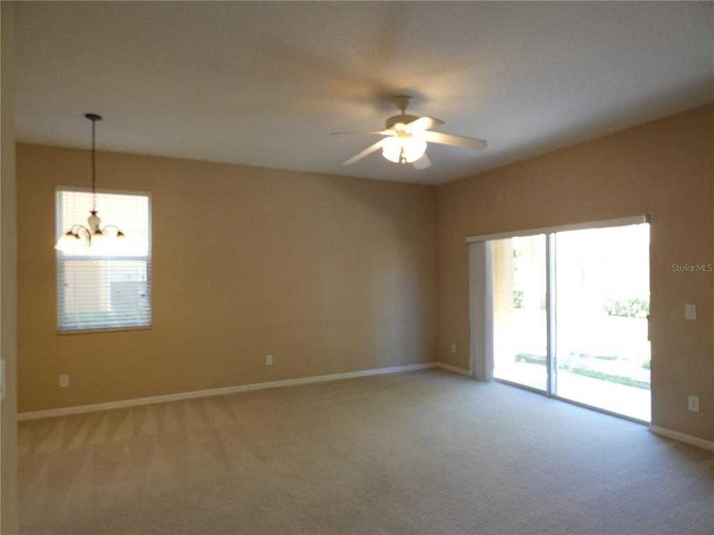 An empty room with beige carpet, tan walls, a ceiling fan, and sliding glass doors — 2111 RETREAT VIEW CIRCLE, SANFORD, FL