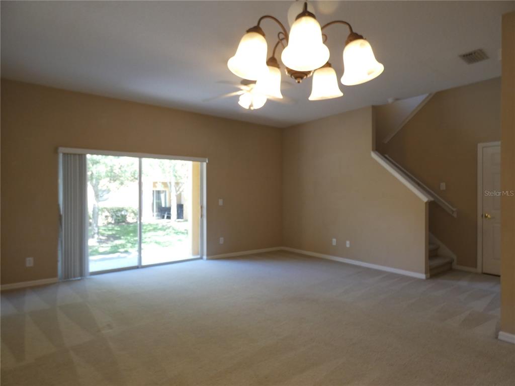 An empty living room features beige carpet, tan walls, a chandelier, and sliding glass doors — 2111 RETREAT VIEW CIRCLE, SANFORD, FL