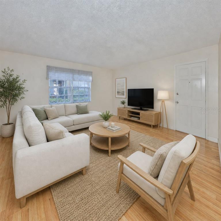 This virtually staged living room features a sectional sofa, armchair, coffee table, and television — 4315 AEGEAN DRIVE UNIT 102C, TAMPA, FL