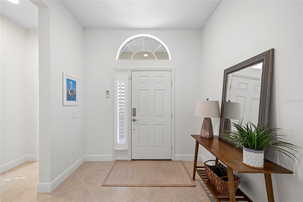 A bright entryway features a white front door, tile flooring, a console table, and a mirror — 4623 CLAREMONT PARK DRIVE, BRADENTON, FL