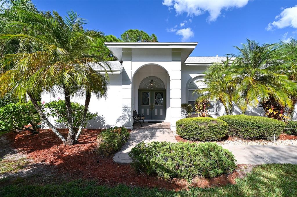 A white house exterior features a covered arched entryway with double doors and palm trees — 3866 SURREY COURT, SARASOTA, FL
