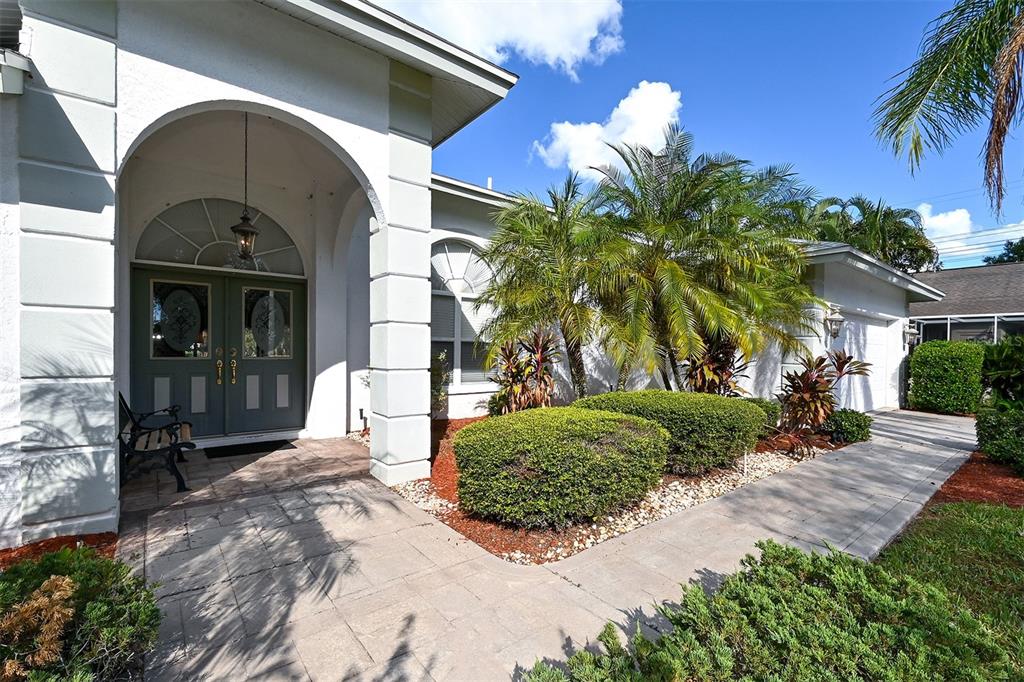 A white house exterior features a covered arched entryway, double front doors, and landscaped bushes — 3866 SURREY COURT, SARASOTA, FL