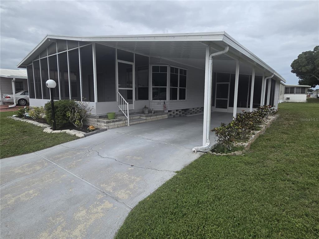 A manufactured home with a screened-in porch, a concrete driveway, and a covered carport — 5707 45TH STREET E UNIT 120, BRADENTON, FL
