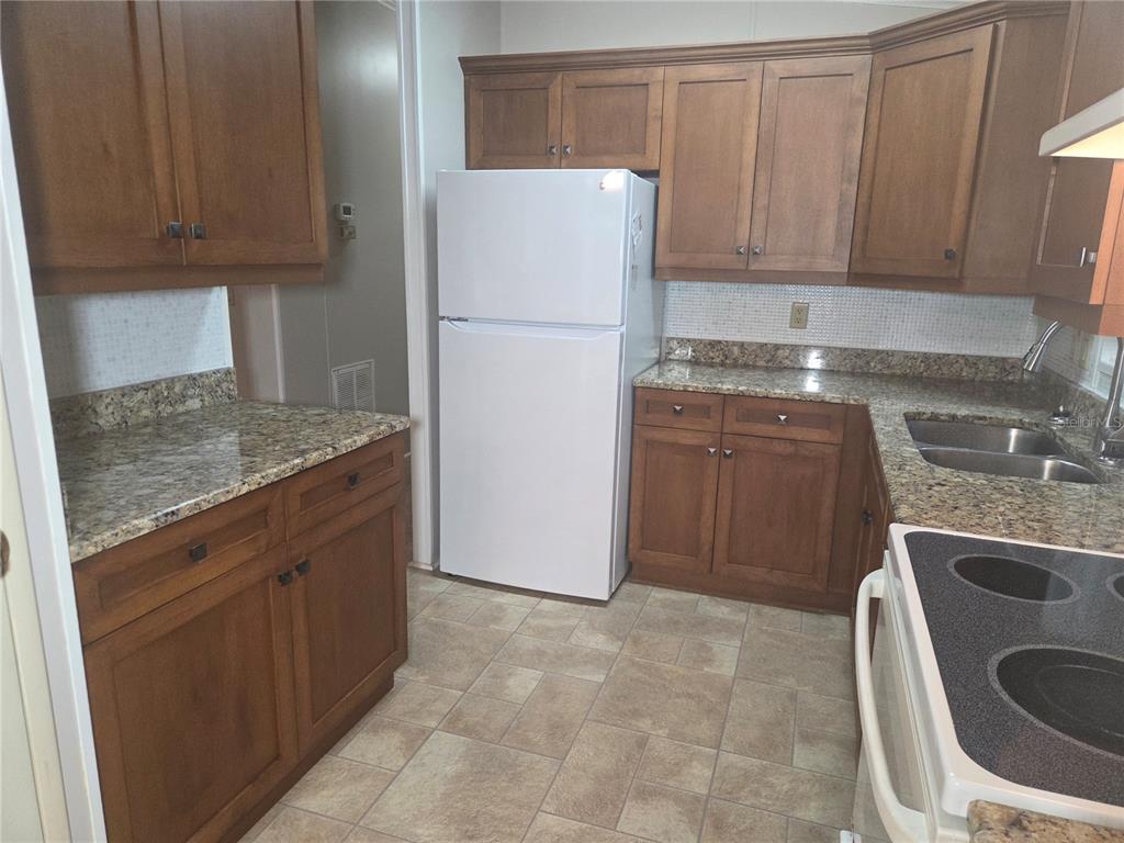 A kitchen features wood cabinets, granite countertops, a white refrigerator, and a tiled floor — 5707 45TH STREET E UNIT 120, BRADENTON, FL