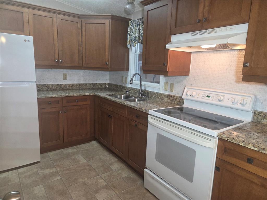 A kitchen features wood cabinets, granite countertops, a white stove, and a white refrigerator — 5707 45TH STREET E UNIT 120, BRADENTON, FL