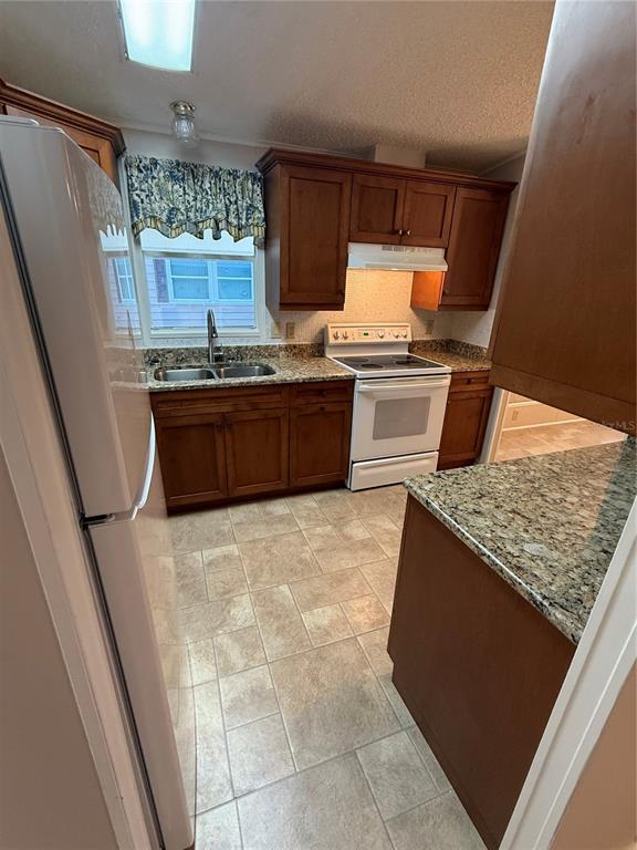 A kitchen features wood cabinets, granite countertops, a white stove, and tile flooring — 5707 45TH STREET E UNIT 120, BRADENTON, FL