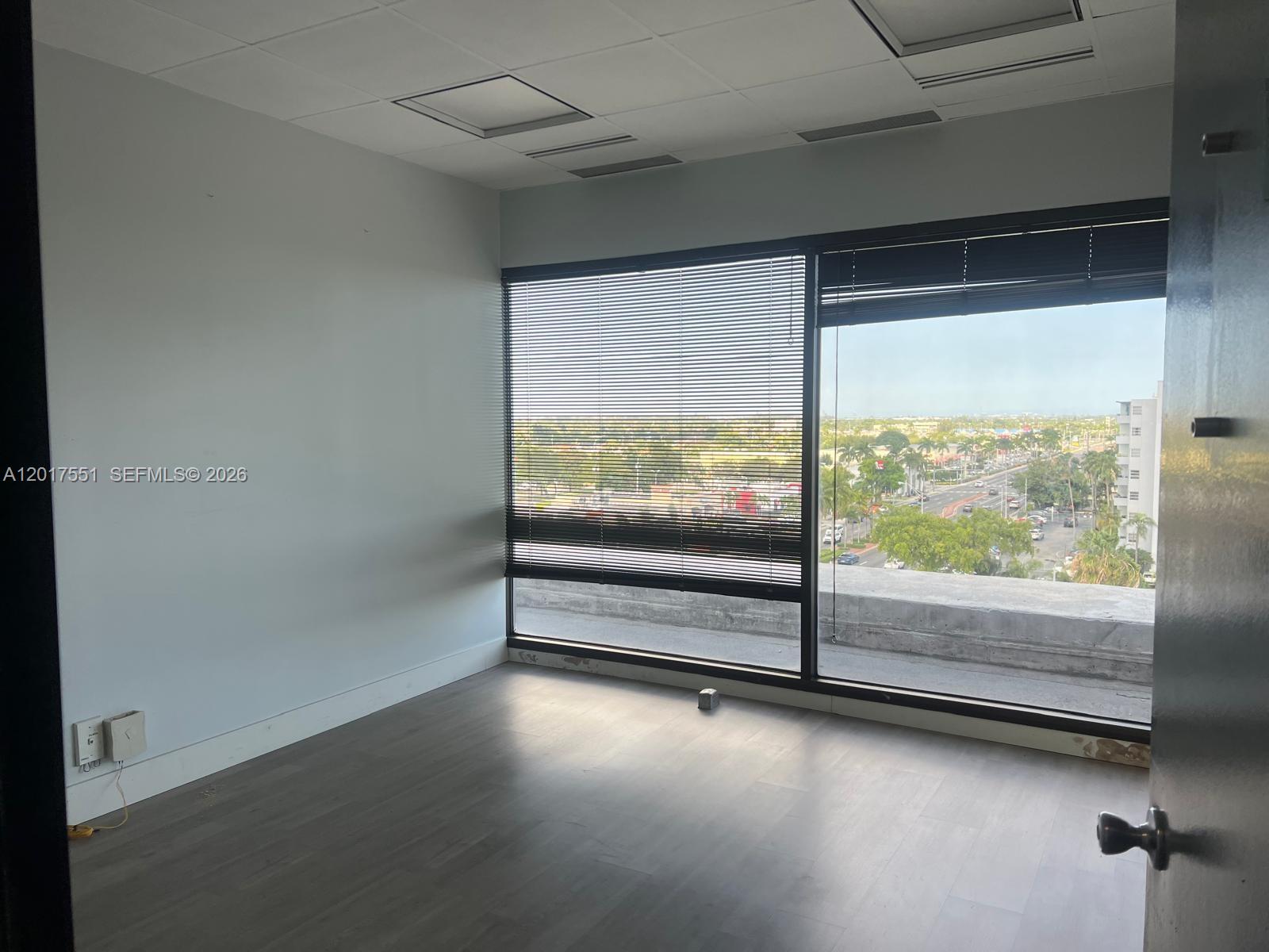 An empty office room features gray wood-look flooring, white walls, and large windows with blinds — 900 W 49th St Suite546, Hialeah FL 33012, HIALEAH, FL