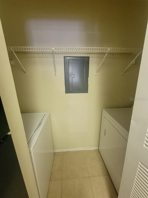A laundry closet contains a white washer and dryer beneath a wire shelf and electrical panel — 10024 STRAFFORD OAK COURT UNIT 813, TAMPA, FL