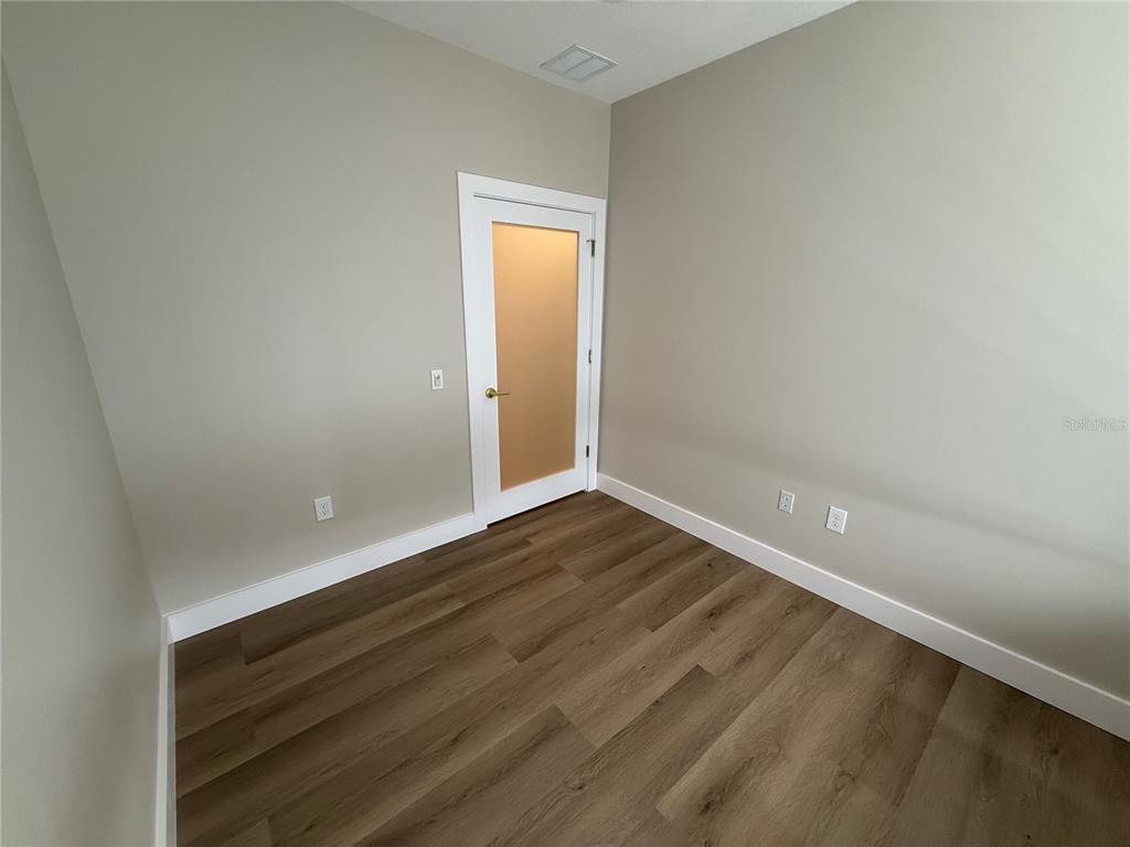 An empty room features light-colored walls, white trim, and wood-look flooring with a frosted glass door — 3699 AIRFIELD DRIVE W, LAKELAND, FL