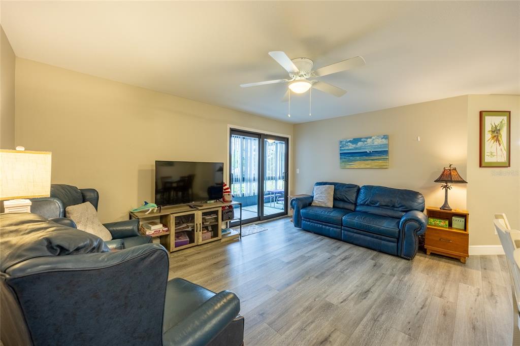 A living room features blue leather sofas, wood-look flooring, a ceiling fan, and sliding doors — 17426 BIRCHWOOD LANE UNIT 1, FORT MYERS, FL