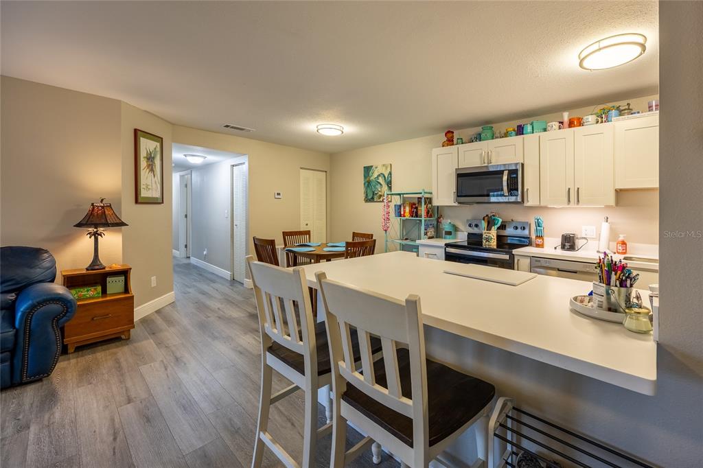 A kitchen with white cabinets and a breakfast bar overlooks a dining area and hallway — 17426 BIRCHWOOD LANE UNIT 1, FORT MYERS, FL