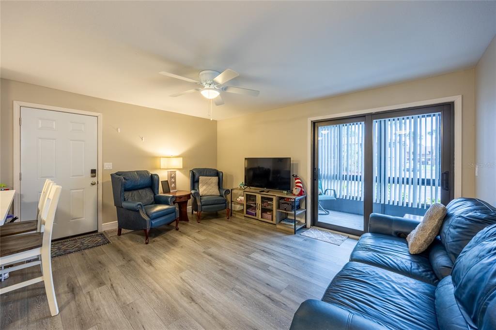 A living room features blue leather furniture, wood-look flooring, a ceiling fan, and sliding doors — 17426 BIRCHWOOD LANE UNIT 1, FORT MYERS, FL