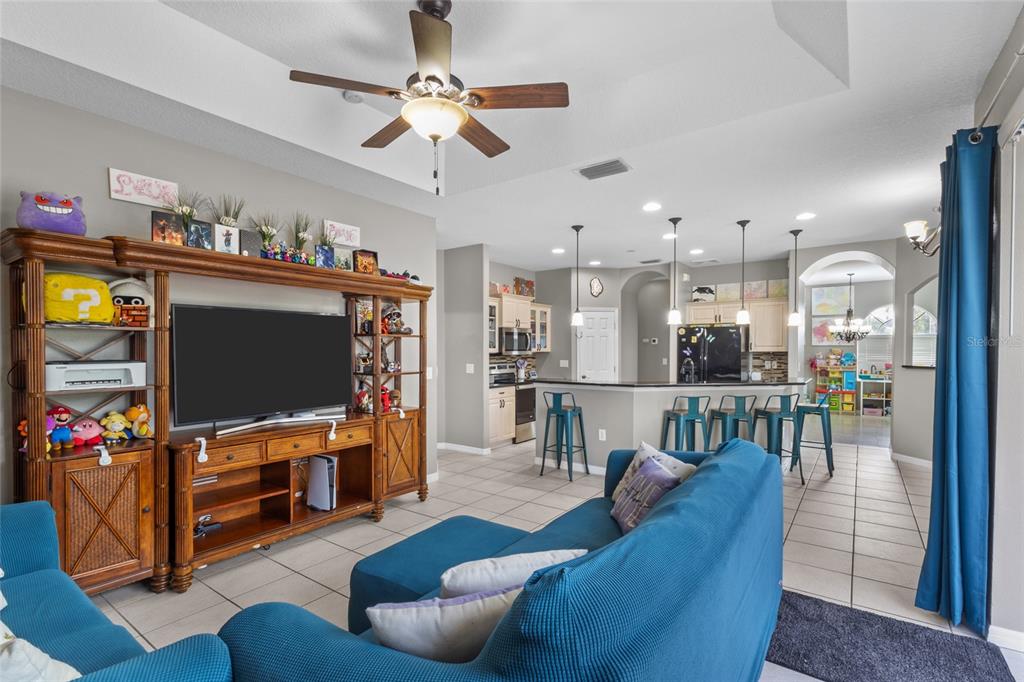 A living room with a blue sofa and wooden entertainment center opens to a kitchen — 111 141ST COURT NE, BRADENTON, FL