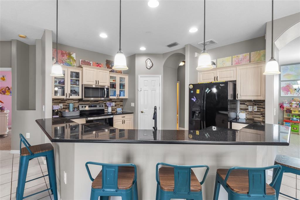 A kitchen features light wood cabinets, black countertops, a black refrigerator, and three blue stools — 111 141ST COURT NE, BRADENTON, FL