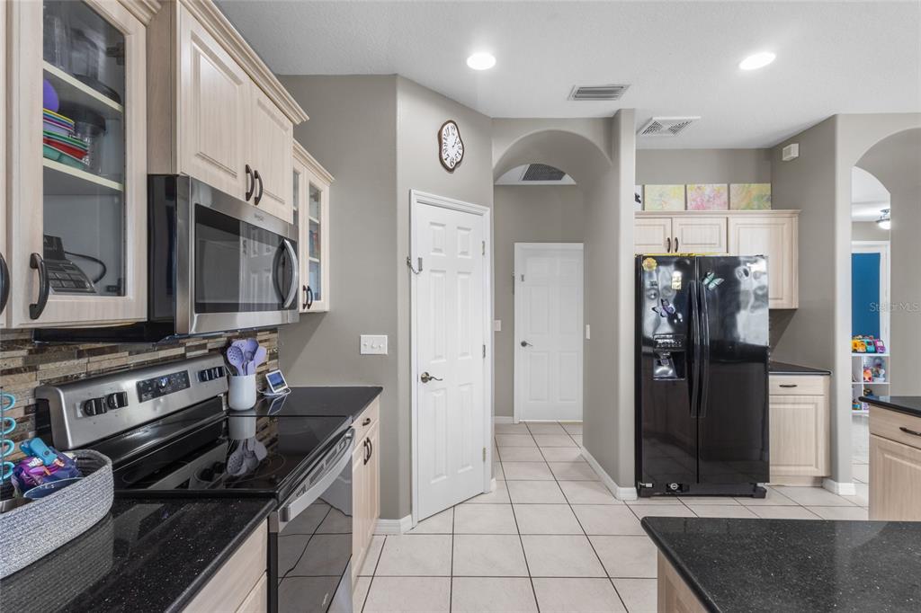 A kitchen features light wood cabinets, black appliances, dark countertops, and tile flooring — 111 141ST COURT NE, BRADENTON, FL