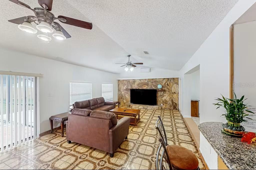 A living room features a stone fireplace, brown leather furniture, and patterned tile flooring — 6223 TRAVIS BOULEVARD, TAMPA, FL