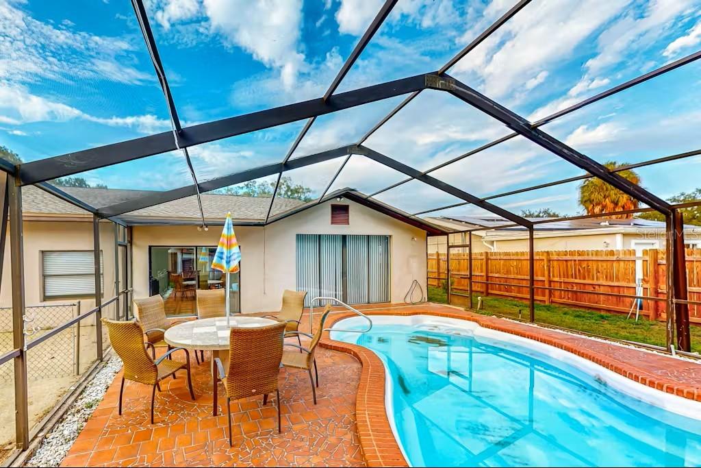 A screened-in patio features a kidney-shaped swimming pool, a dining set, and brick pavers — 6223 TRAVIS BOULEVARD, TAMPA, FL