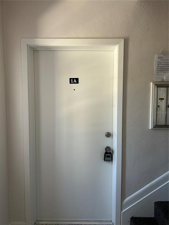 A white apartment door labeled 1A with a digital lock is set in a plain wall — 7011 PLACE DE LA PAIX UNIT 1A, ST PETERSBURG, FL