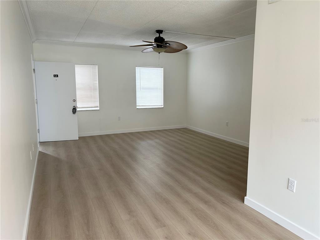 An empty room features light wood-look flooring, white walls, two windows, and a ceiling fan — 7011 PLACE DE LA PAIX UNIT 1A, ST PETERSBURG, FL