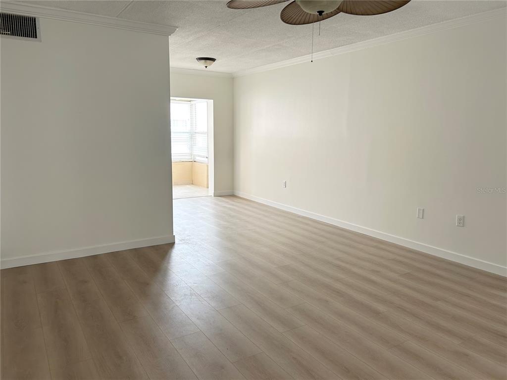 An empty living room features light wood-look flooring, white walls, and a ceiling fan — 7011 PLACE DE LA PAIX UNIT 1A, ST PETERSBURG, FL