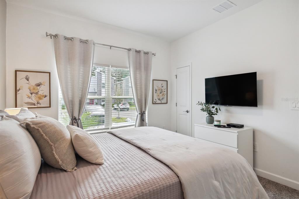 A bedroom features a bed with neutral bedding, a wall-mounted television, and a window view — 2440 READING TRAIL, KISSIMMEE, FL