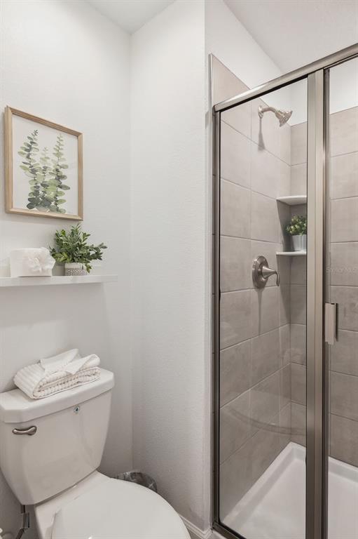 A bathroom features a white toilet, a floating shelf with decor, and a glass-enclosed shower — 2440 READING TRAIL, KISSIMMEE, FL