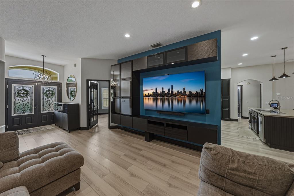 A living room features a large wall-mounted television, dark cabinetry, and light wood-look flooring — 1808 TANGLEDVINE DRIVE, WESLEY CHAPEL, FL