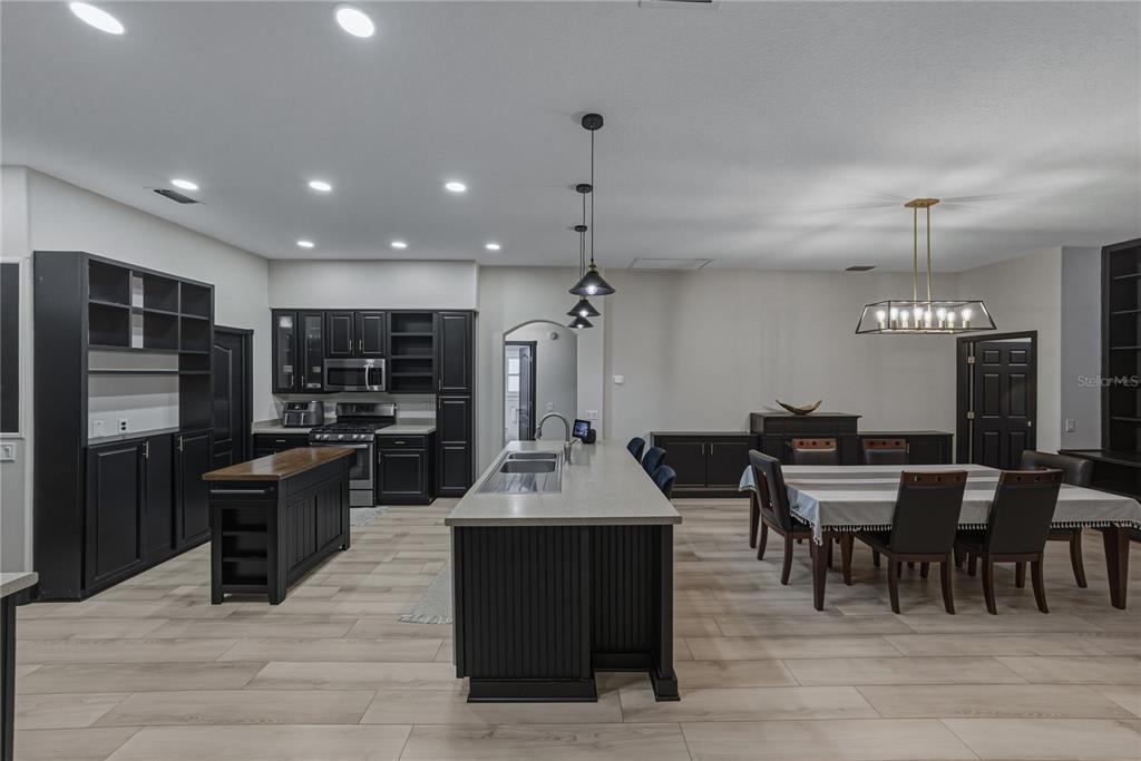A kitchen and dining area featuring dark cabinetry, a central island, and light wood flooring — 1808 TANGLEDVINE DRIVE, WESLEY CHAPEL, FL
