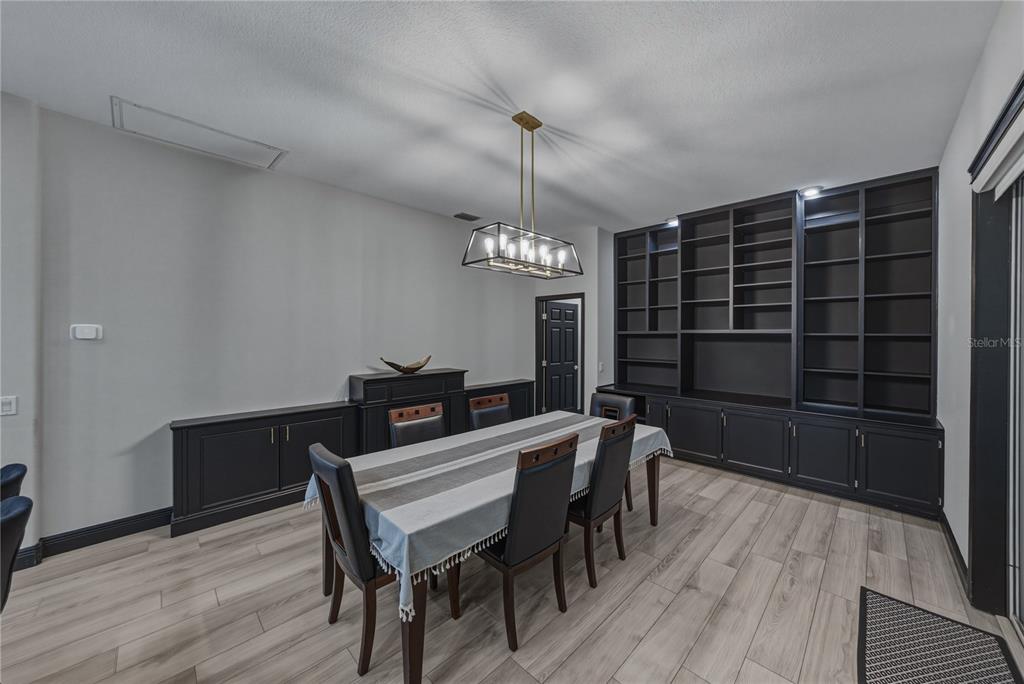 A dining room features dark built-in cabinetry, a rectangular table with chairs, and a chandelier — 1808 TANGLEDVINE DRIVE, WESLEY CHAPEL, FL